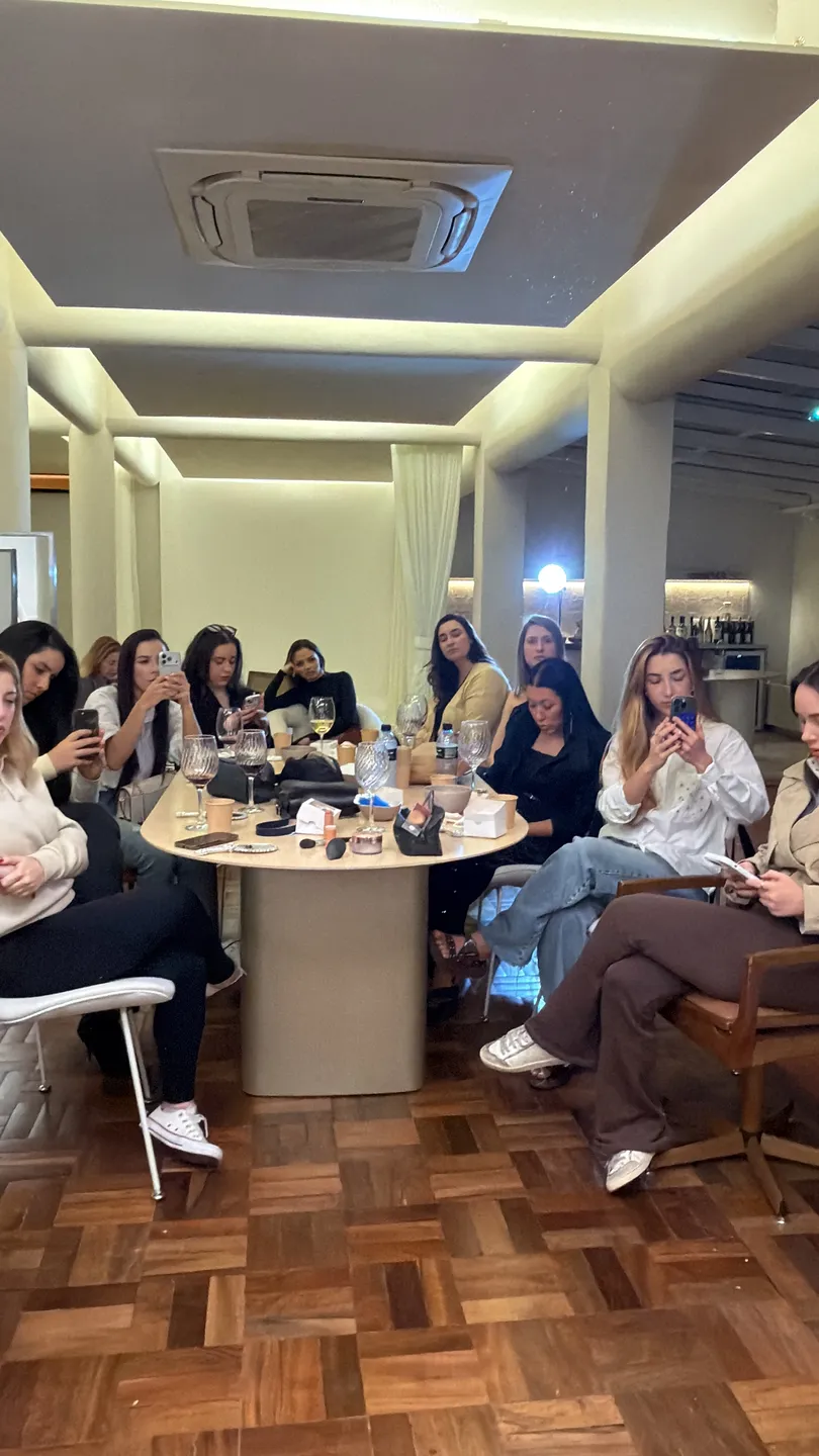 Mulheres em volta da mesa, taças na mão, registrando o encontro