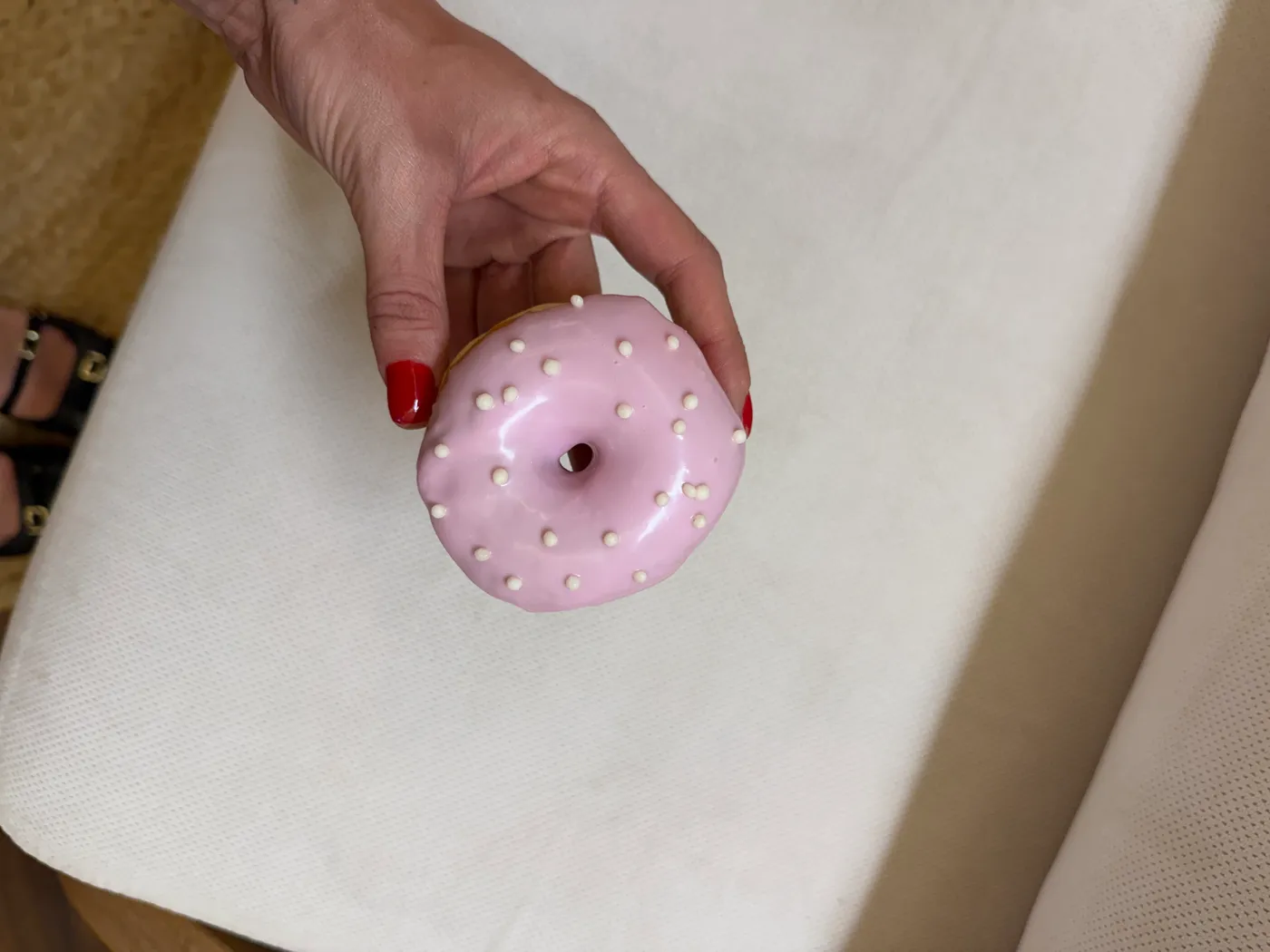 Mão de unhas vermelhas segurando um donut rosa