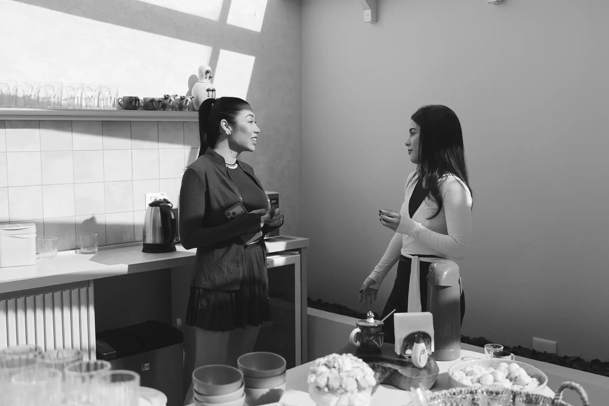 Duas mulheres preparando algo no balcão (preto e branco)